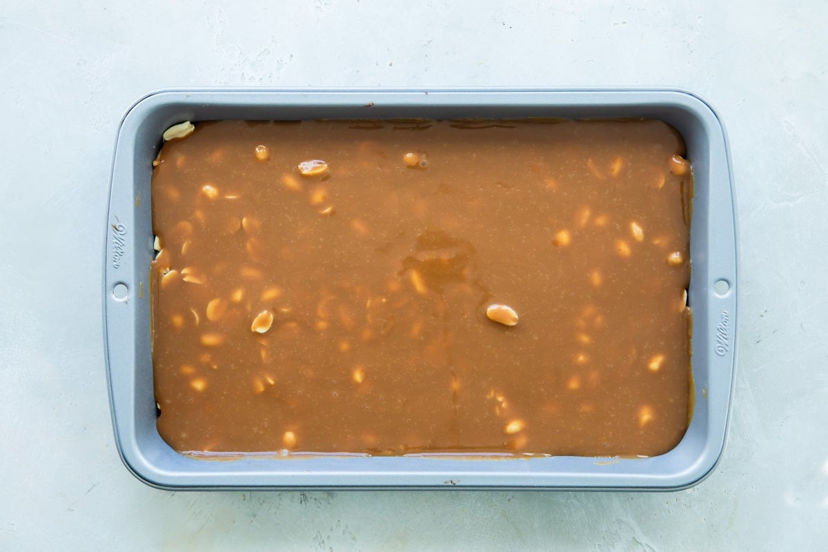 Caramel spread out over nougat and peanut layer in a baking pan.