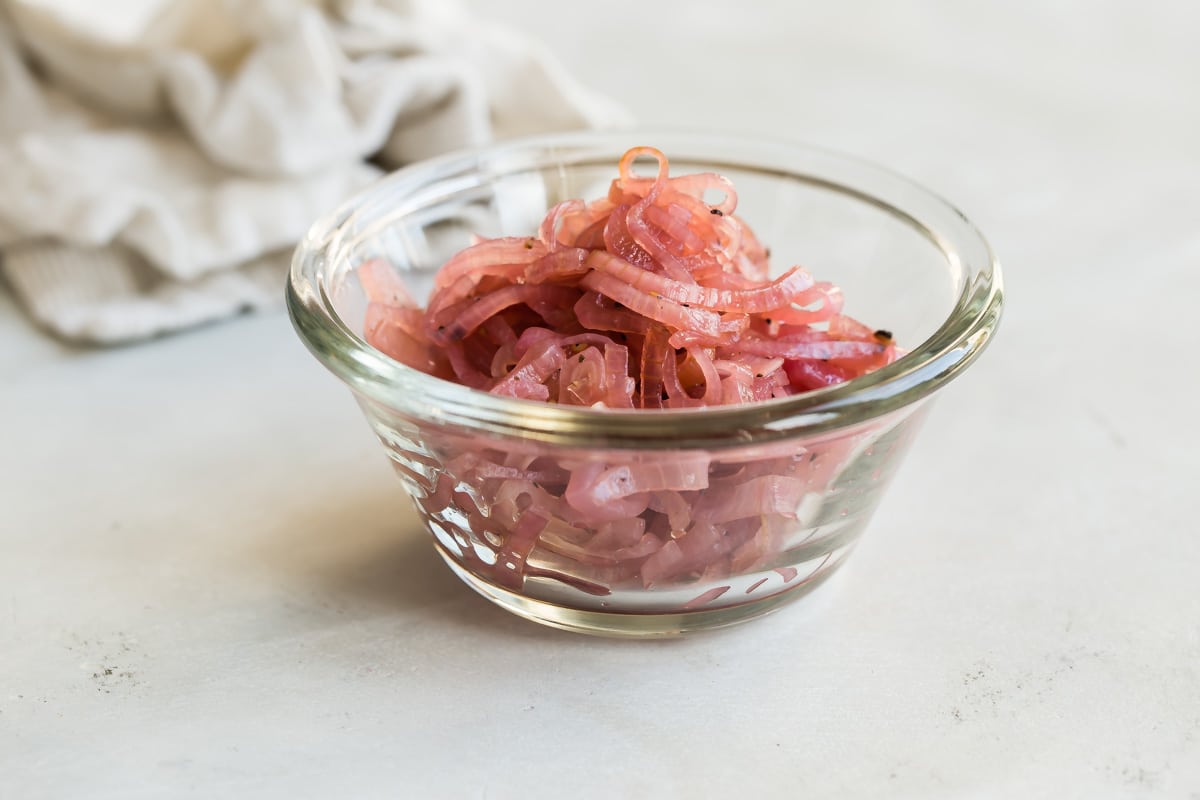 Pickled shallots in a small clear bowl.