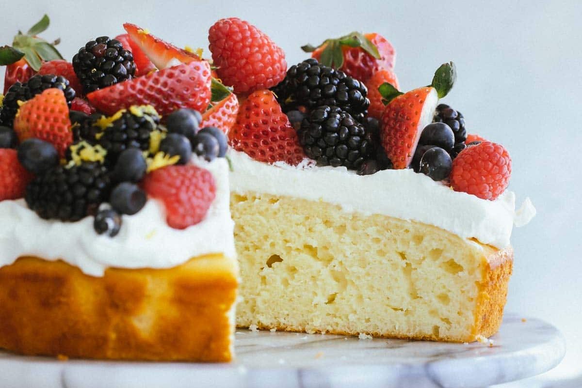 Lemon cake with limoncello cream and berries on top on a marble cake stand.
