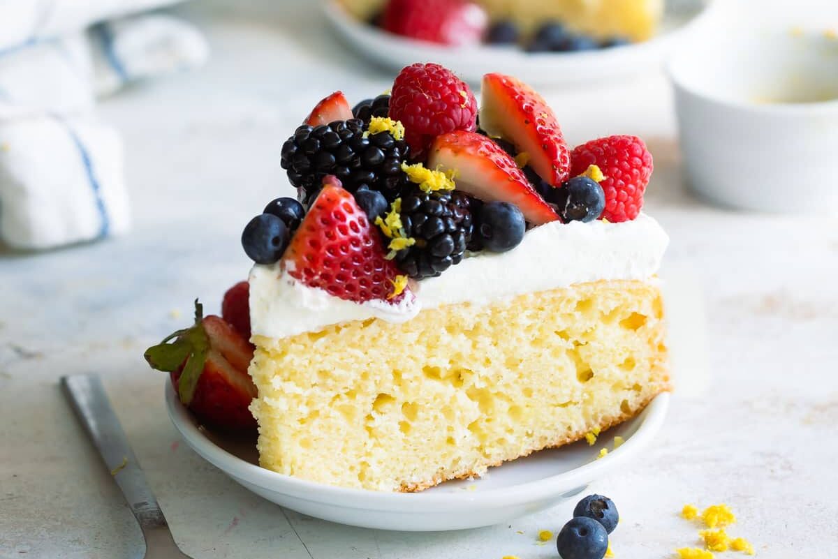 Two slices of lemon cake with limoncello cream and berries on plates.
