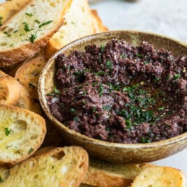 Homemade olive tapenade in a bowl surrounded by toasted bread.