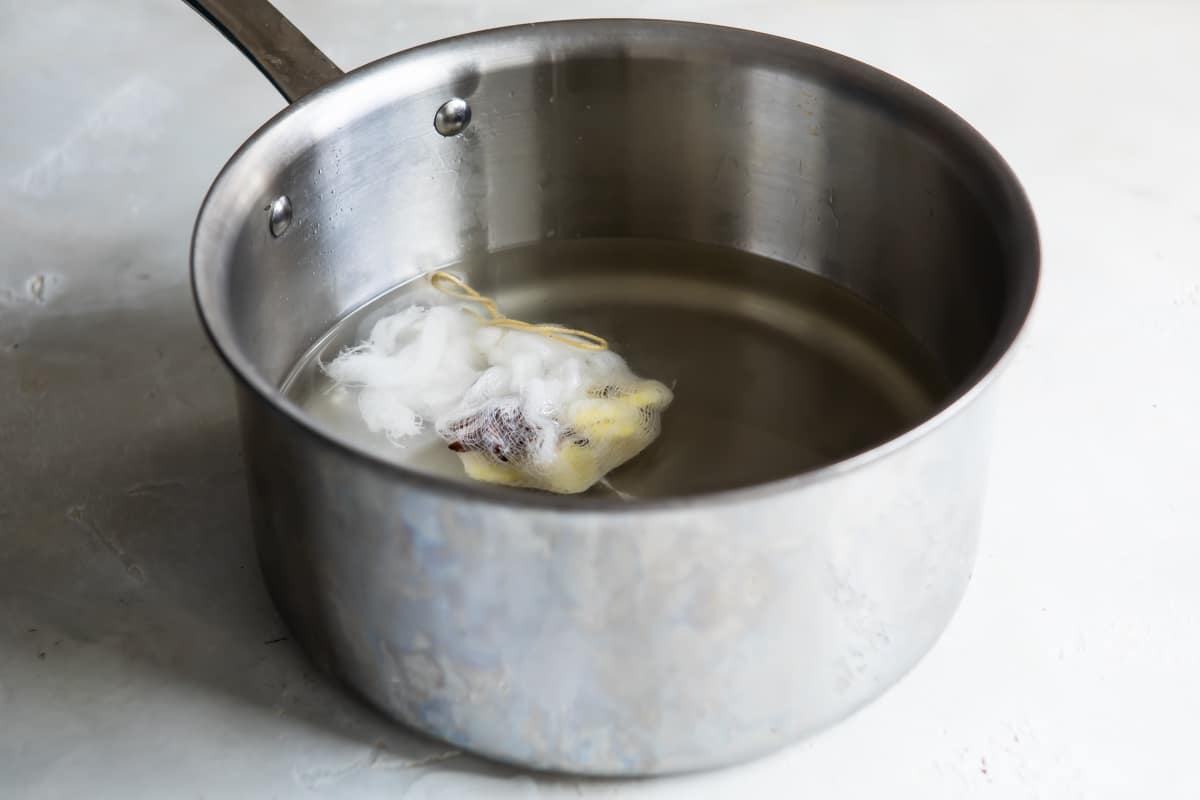 A cheesecloth sack sitting in a yellow liquid in a saucepan.