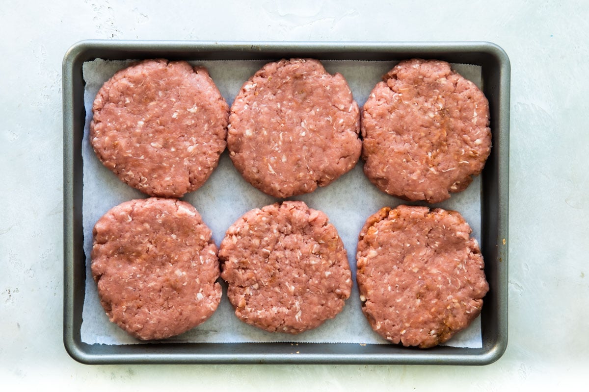Pork burgers on a baking sheet before being cooked.