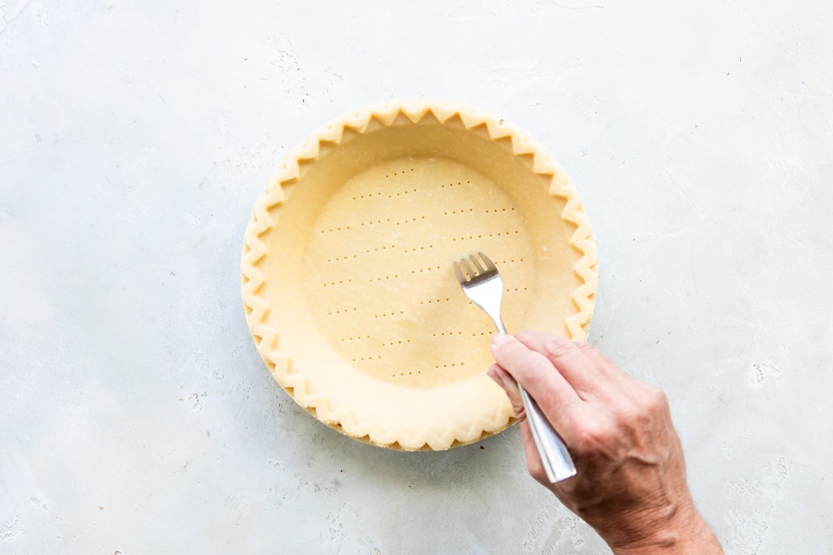 Someone poking holes into a pie crust with a fork.