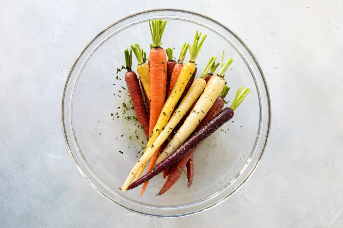 Carrots in a clear bowl with oil and seasoning on them.