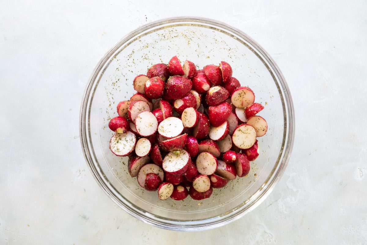 Raw radishes in a bowl with olive oil and spices.