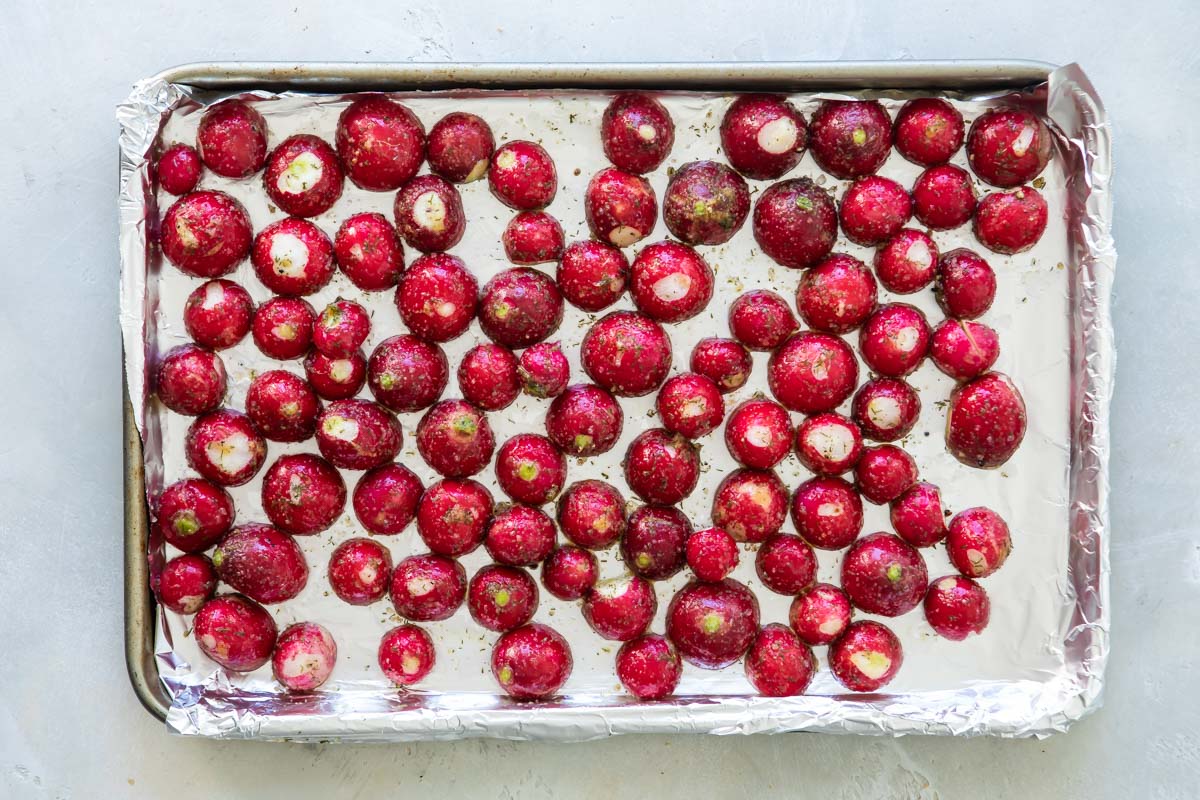Seasoned raw radishes on a baking sheet.