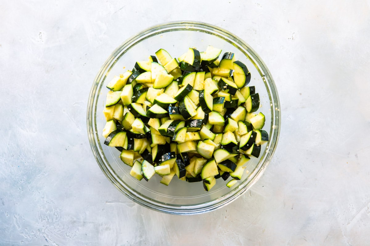 Zucchini pieces covered in oil in a clear bowl.