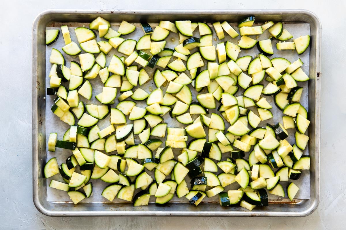 Roasted zucchini on a silver baking sheet before being roasted.