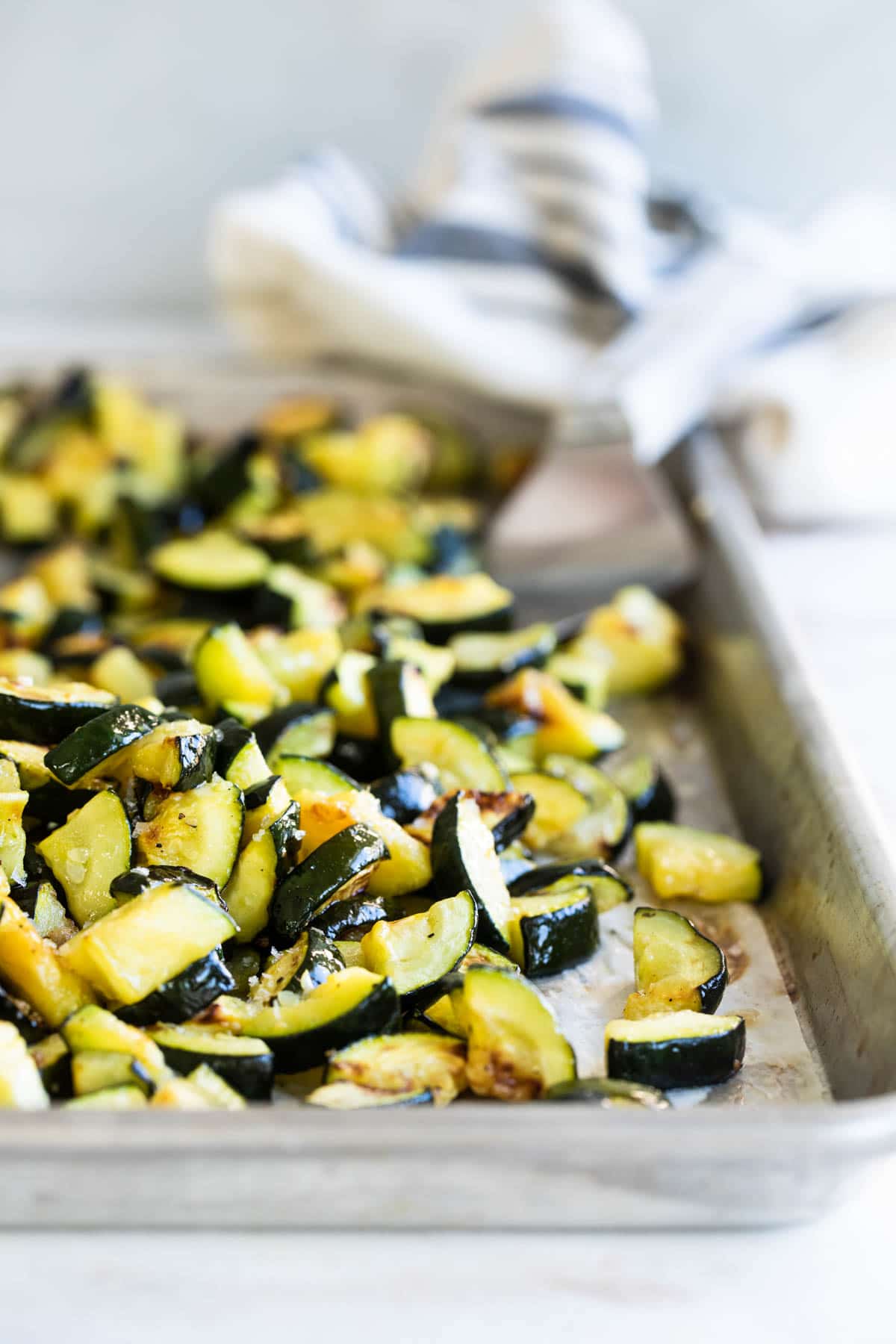 Roasted zucchini on a silver baking sheet.