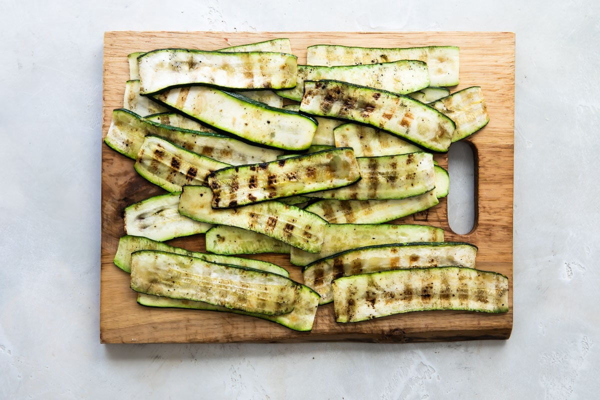 Grilled zucchini slices on a wooden cutting board.