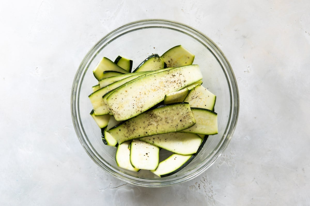 Uncooked zucchini strips in a clear glass bowl.