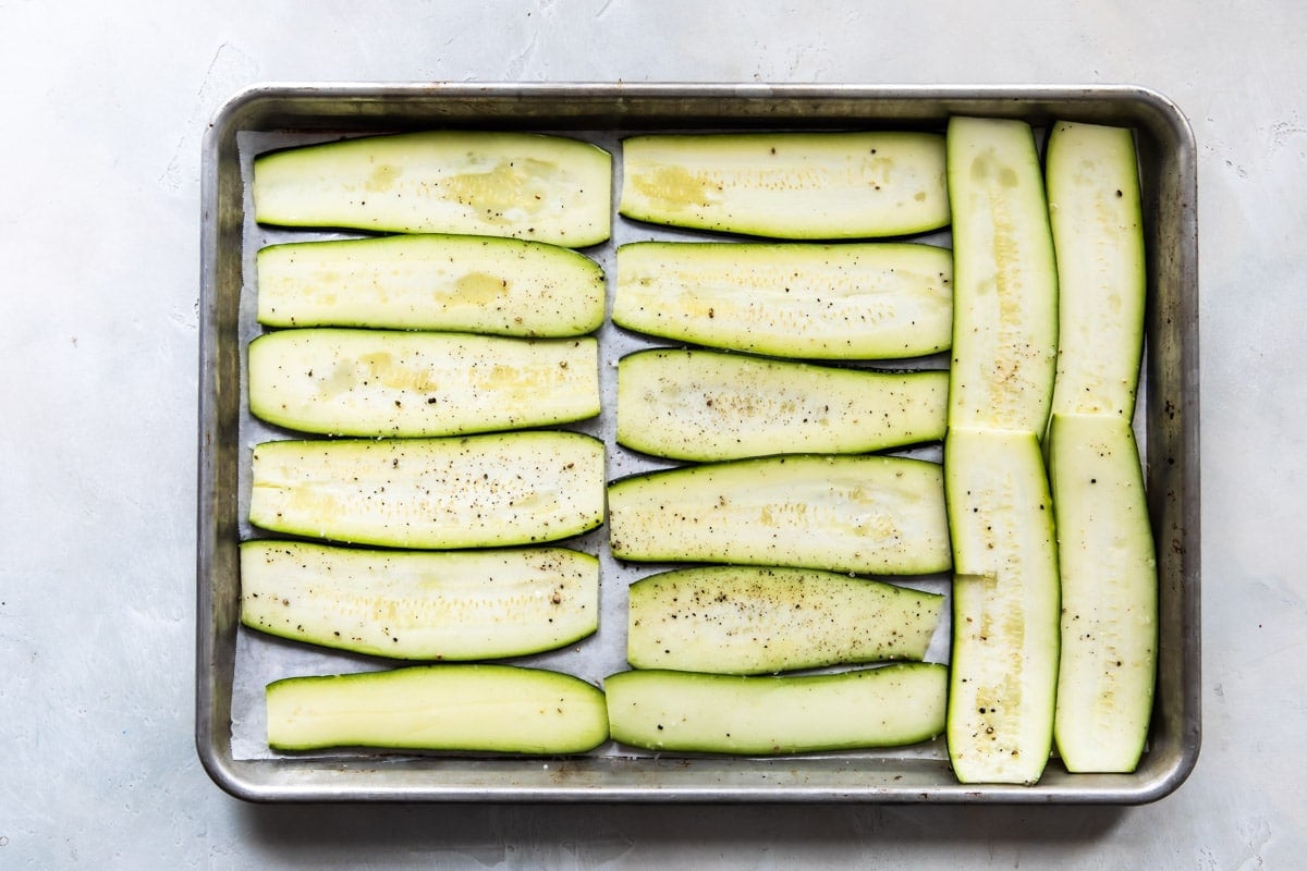 Uncooked zucchini strips on a parchment paper lined baking sheet.