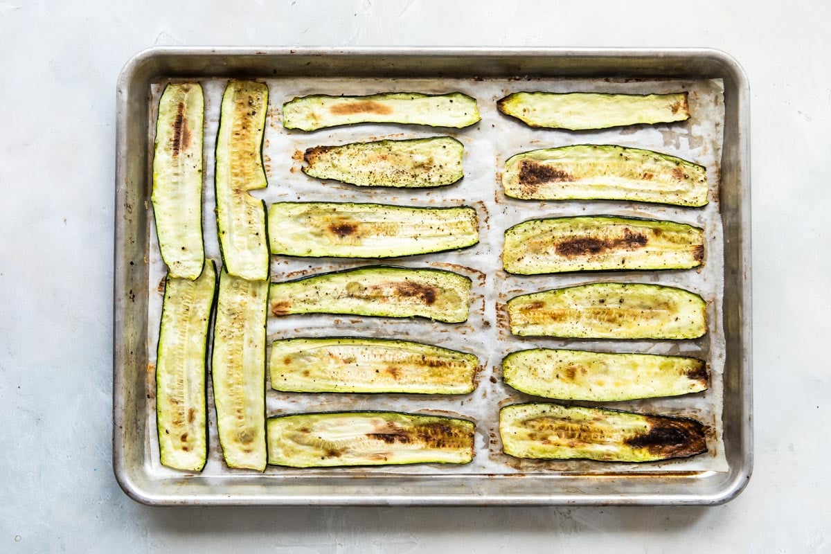 Roasted zucchini strips on a parchment paper lined baking sheet.