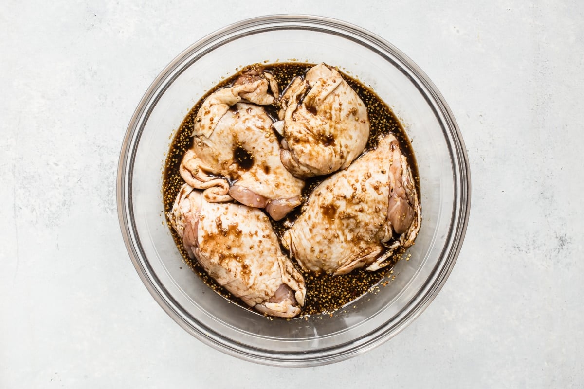 Chicken thighs in a clear bowl marinating.