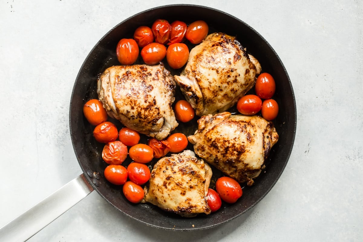 Chicken and tomatoes in a black skillet.