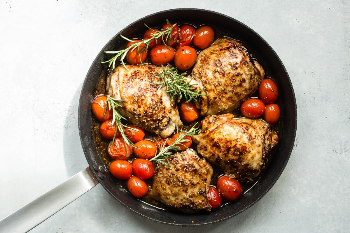 Cooked balsamic chicken and tomatoes in a black skillet.