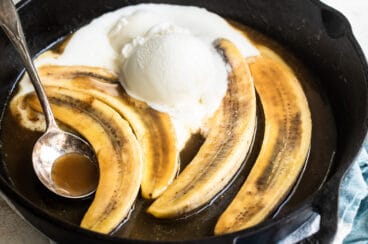 Bananas foster in a black skillet with a serving spoon resting in it.