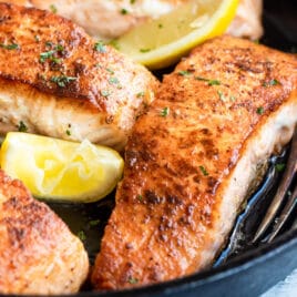 Salmon in a cast iron skillet with lemons for garnish.