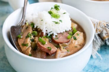 Chicken gumbo in a small white bowl with rice on top.