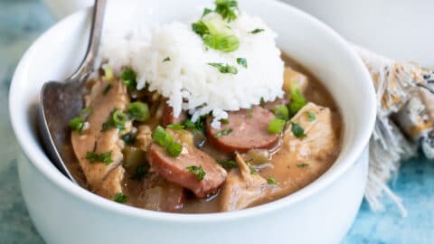 Chicken gumbo in a small white bowl with rice on top.