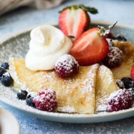 A plate of crepes with whipped cream and berries on top.