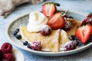A plate of crepes with whipped cream and berries on top.
