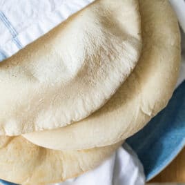 Three pieces of homemade pita bread wrapped in a linen towel on a blue plate.