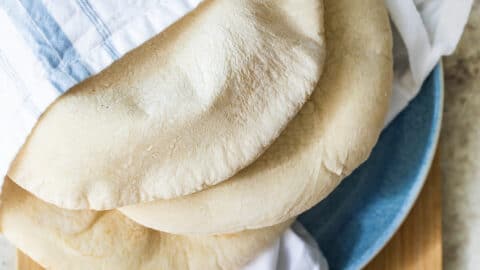 Three pieces of homemade pita bread wrapped in a linen towel on a blue plate.