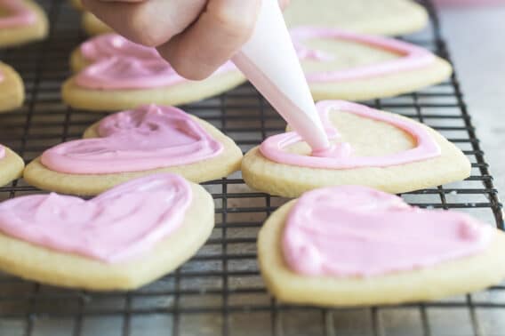 Someone frosting heart sugar cookies with pink royal icing.