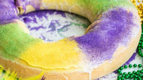 A decorated king cake on a white counter surrounded by Mardi Gras decorations.