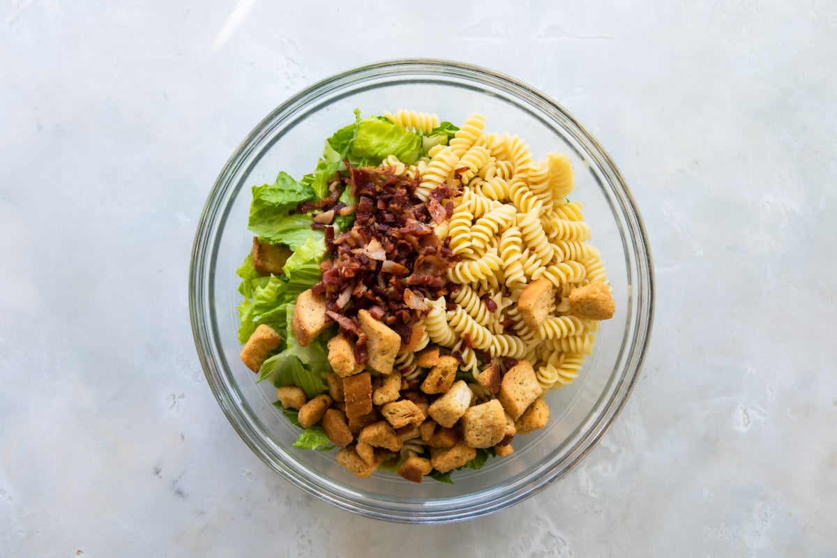 Chicken Caesar pasta salad in a clear bowl before being mixed.