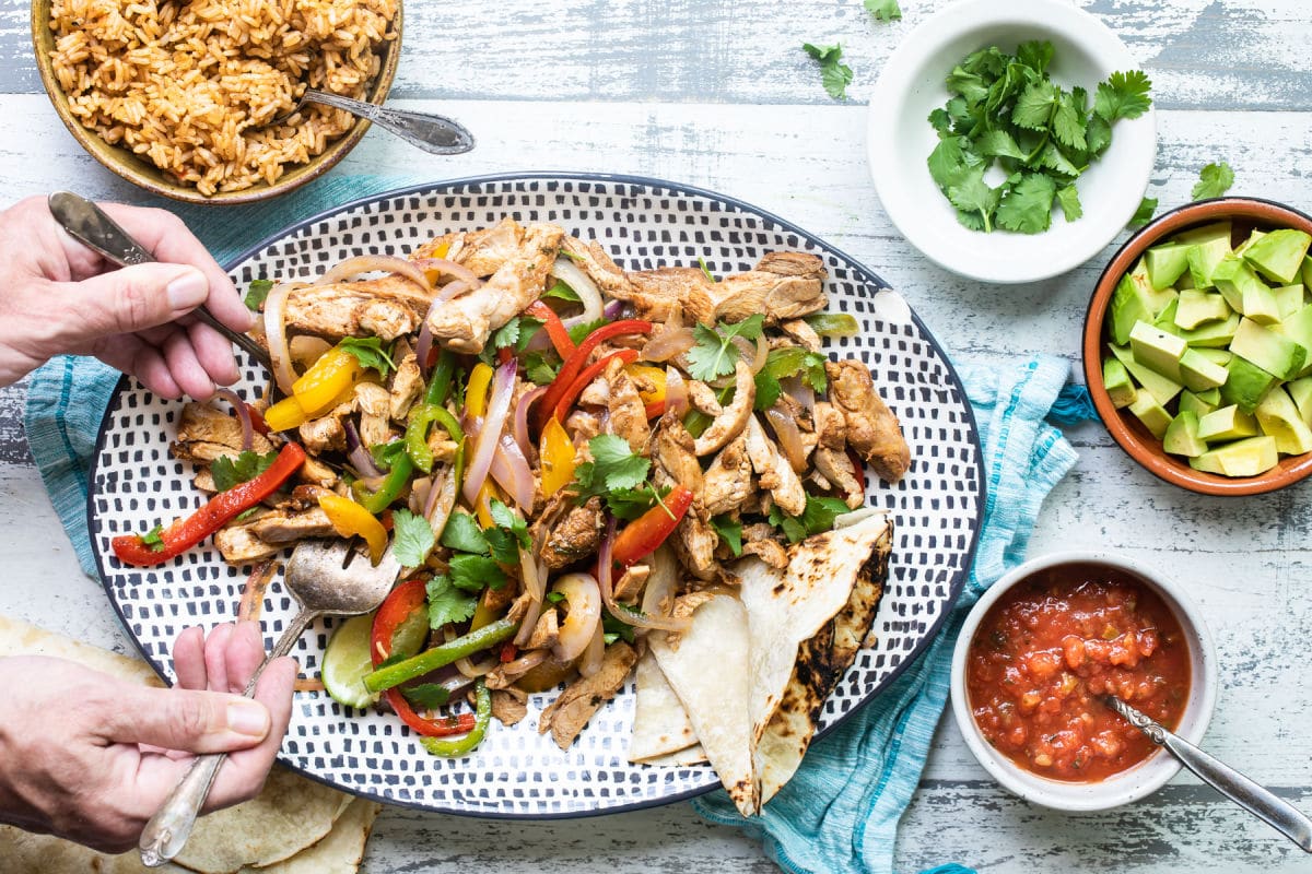 A platter of chicken fajitas with tortillas and toppings on the side.