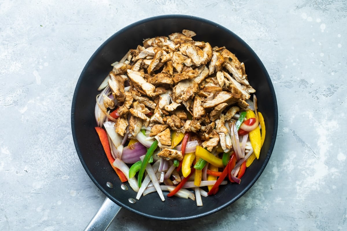 Chicken and veggies in a black skillet.