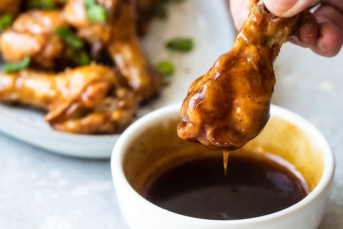 A Coca-Cola chicken wing being dipped in sauce.