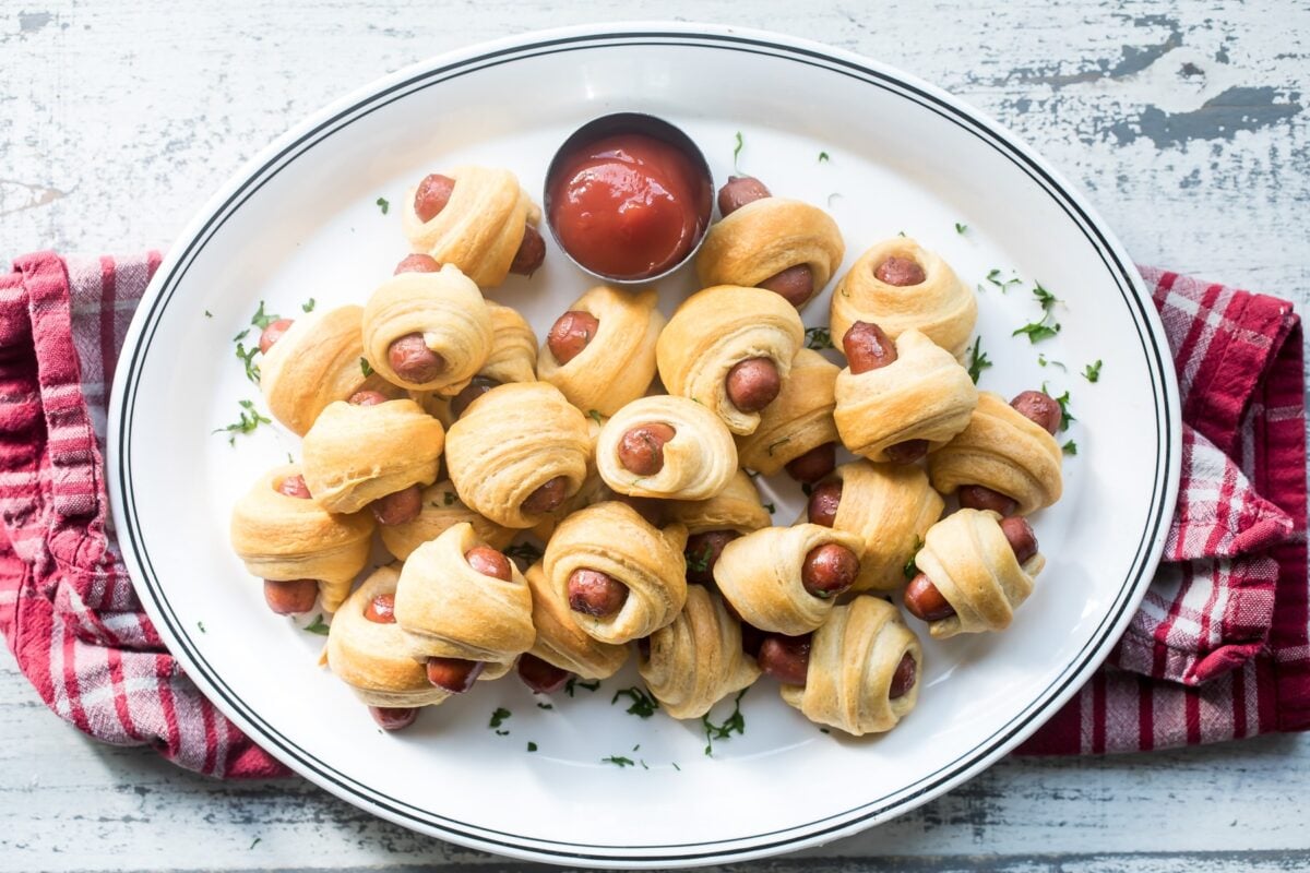 Easy pigs in a blanket on a white plate with a side of ketchup.