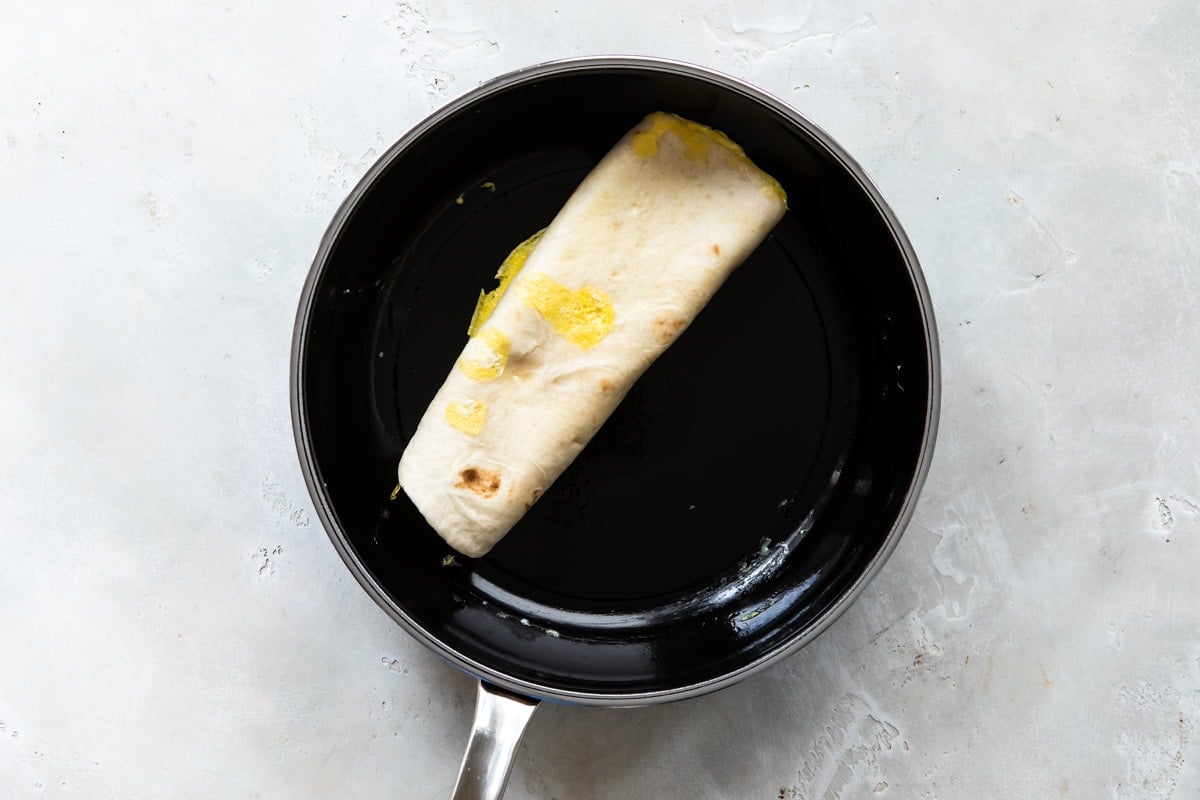 An egg burrito being cooked in a black skillet.