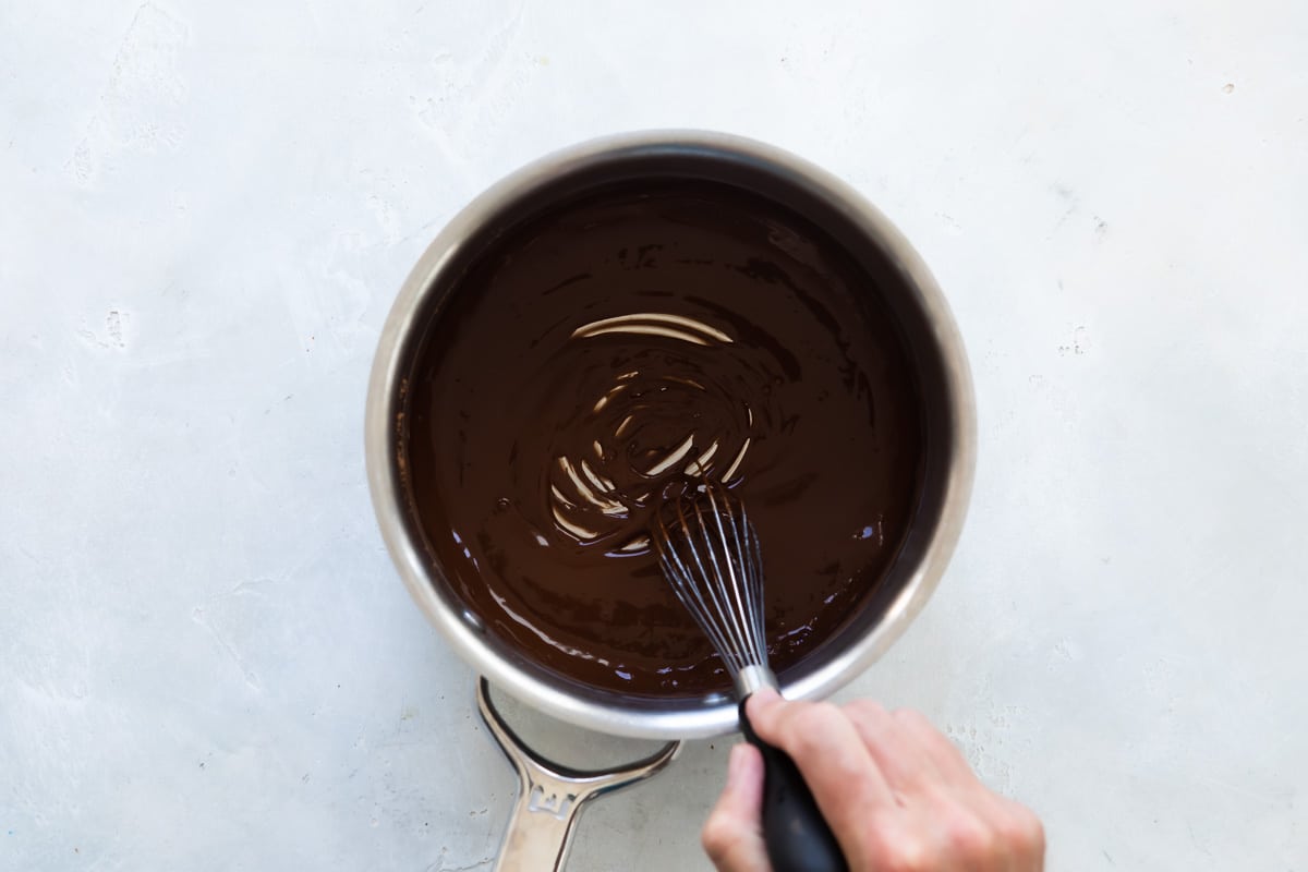 Chocolate sauce being stirred in a silver saucepan.