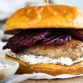 A pork burger with feta mustard and pickled beets on a wooden cutting board.