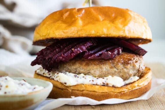 A pork burger with feta mustard and pickled beets on a wooden cutting board.