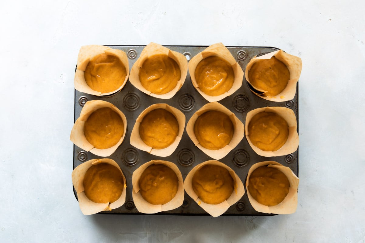 Twelve pumpkin muffins in a muffin tin before being baked.
