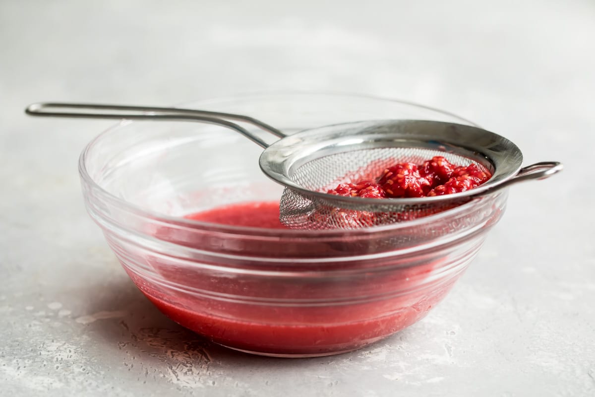 Raspberries in a mesh sieve resting on a clear bowl.
