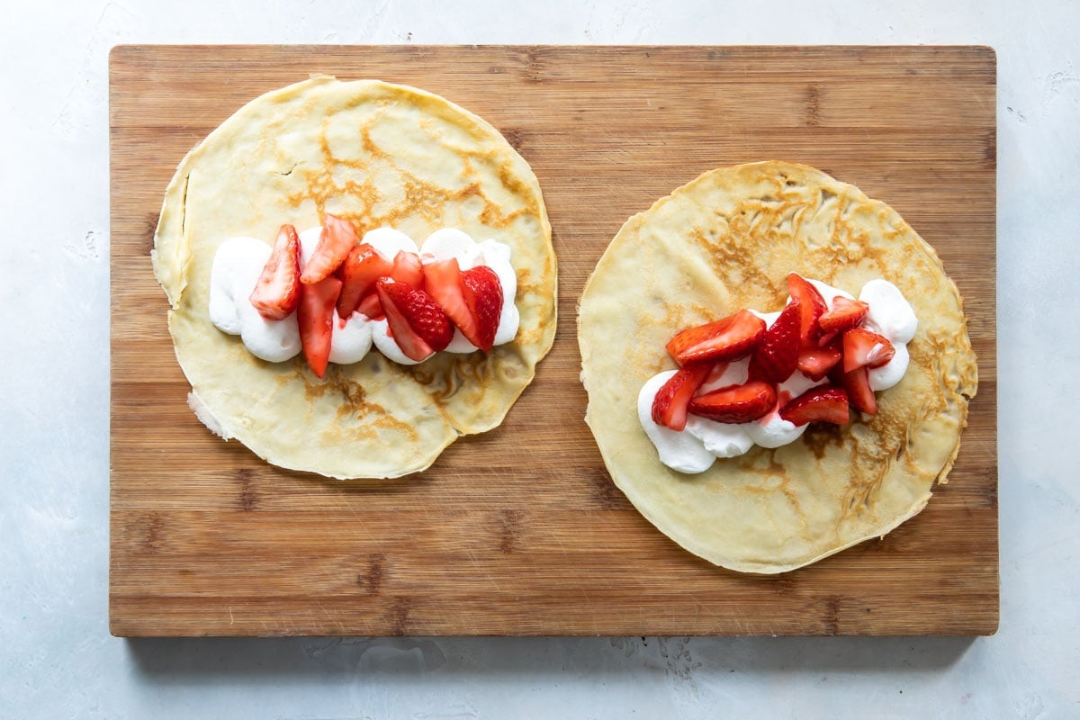 Strawberry crepes on a wooden cutting board.