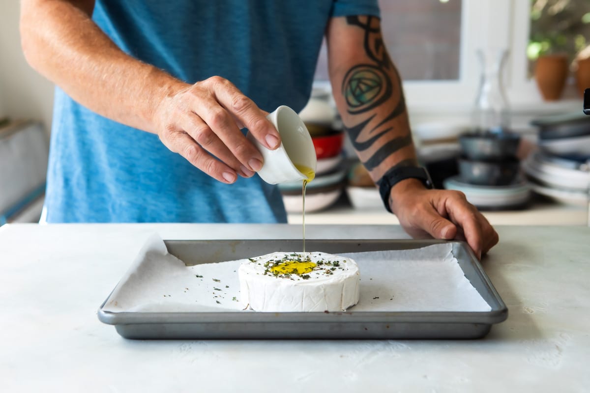 Someone pouring olive oil over brie cheese.