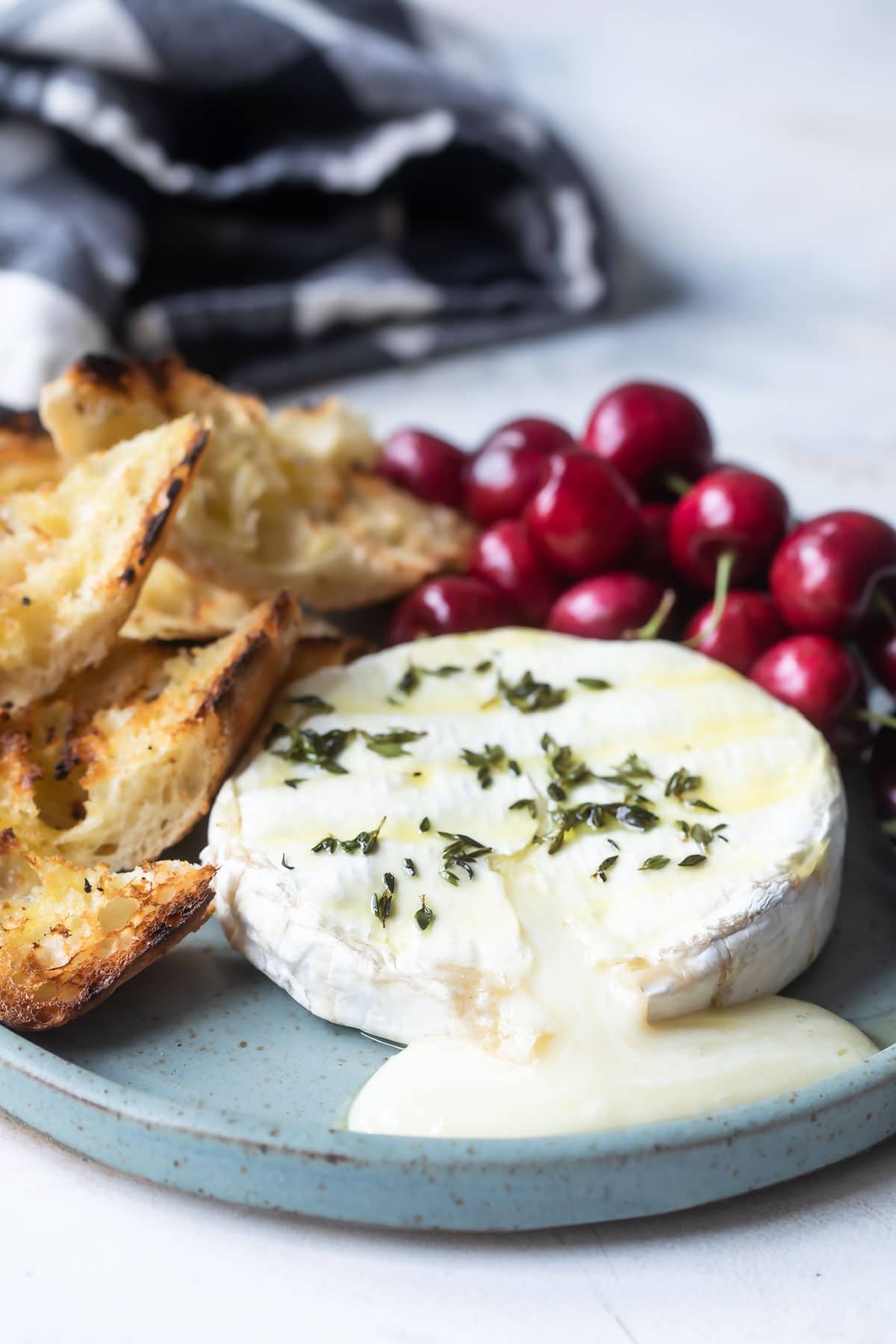 Baked brie on a blue plate with cherries and toasted bread pieces.