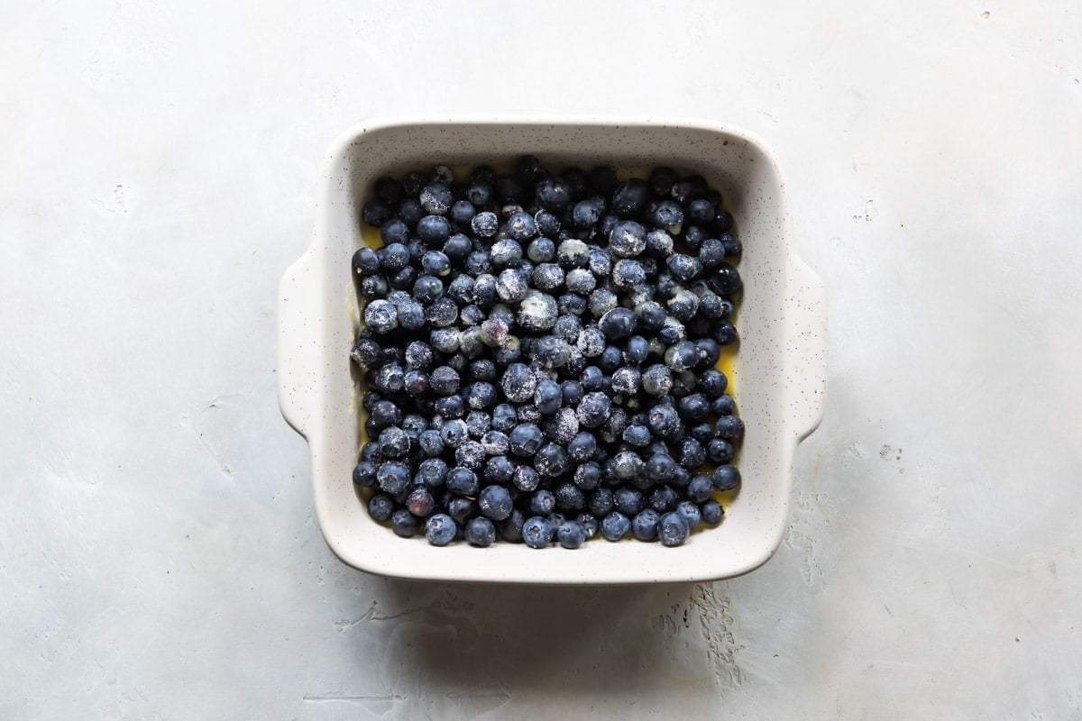 Blueberries and orange juice in a baking dish for blueberry cobbler.
