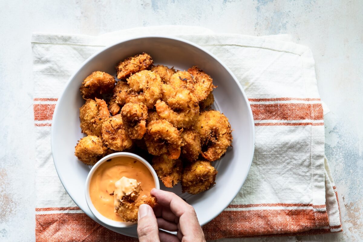 Coconut shrimp being dipped in an orange sauce.