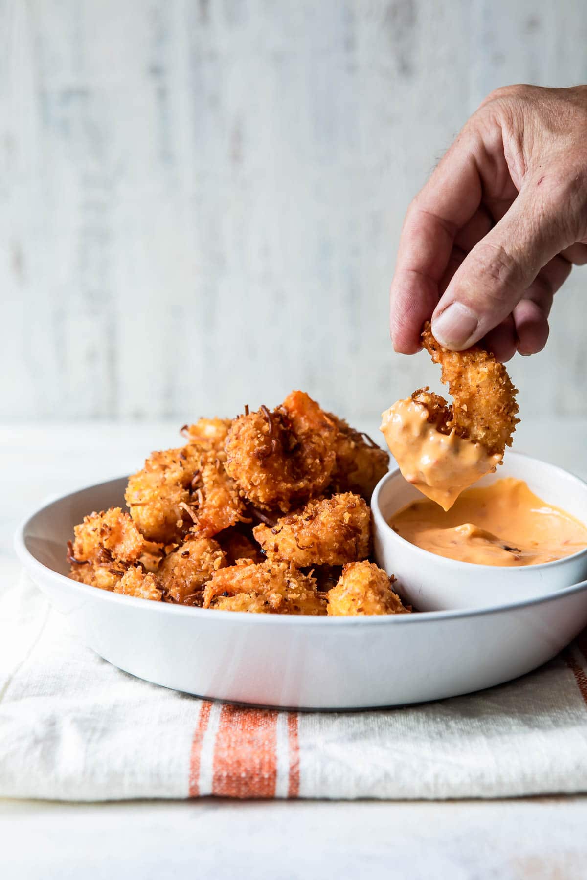 Coconut shrimp being dipped in an orange sauce.