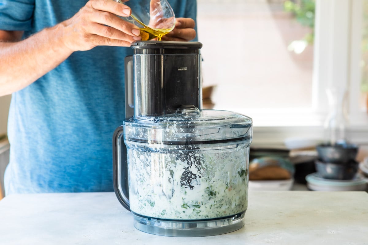 Someone pouring oil into a food processor for cilantro lime dressing.