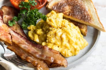 A plate with scrambled eggs, bacon, toast and parsley.